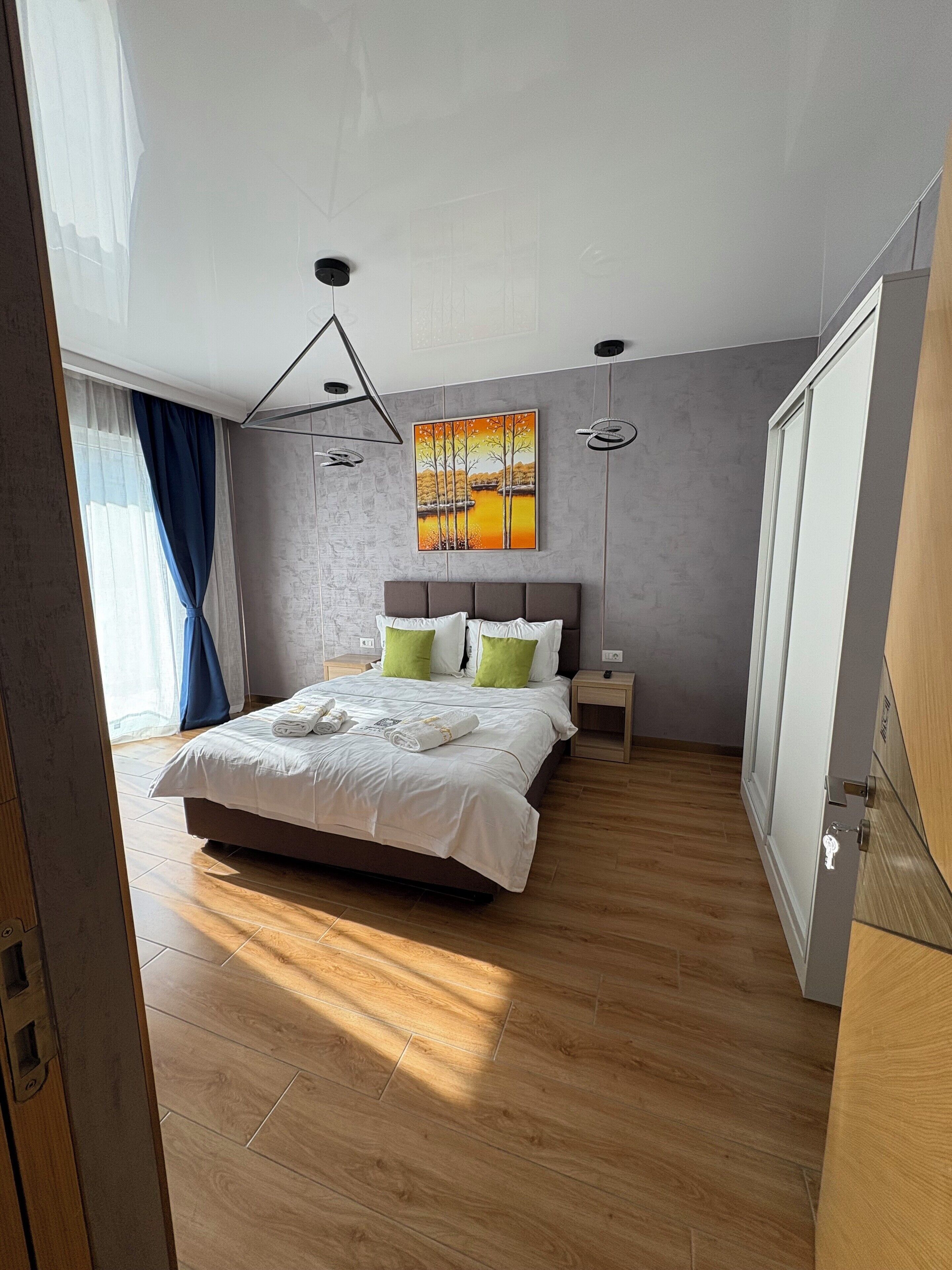 A modern bedroom with a large bed, a painting on the wall, and a wooden floor.