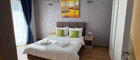 A modern bedroom with a large bed, a painting on the wall, and a wooden floor.
