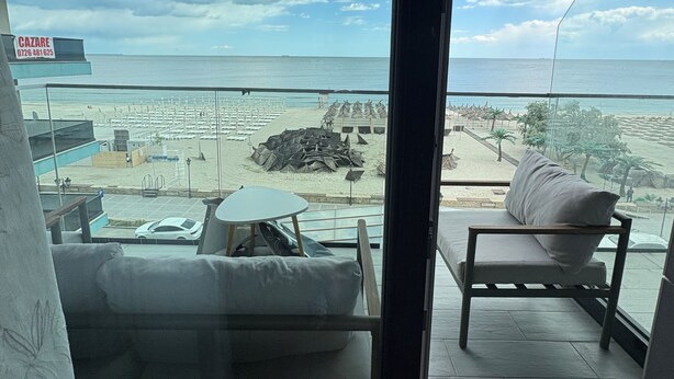 A balcony with a view of the beach, a sofa, a table, and a signboard. - Signature Promenada Hotel-Apartments 2 (Navodari)
