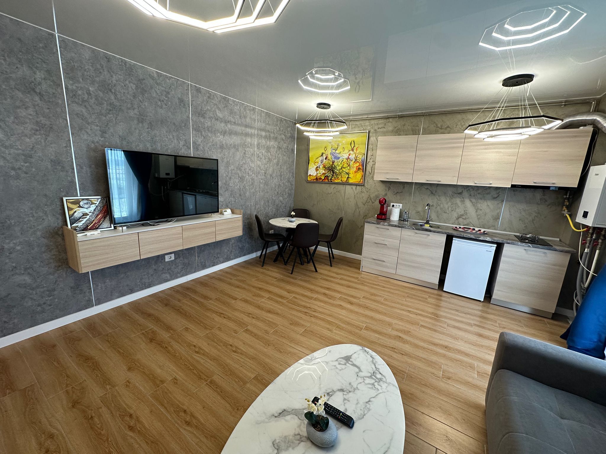Een moderne woonkamer met een flatscreen televisie, een marmeren salontafel en een eethoek met een kleine tafel en stoelen.