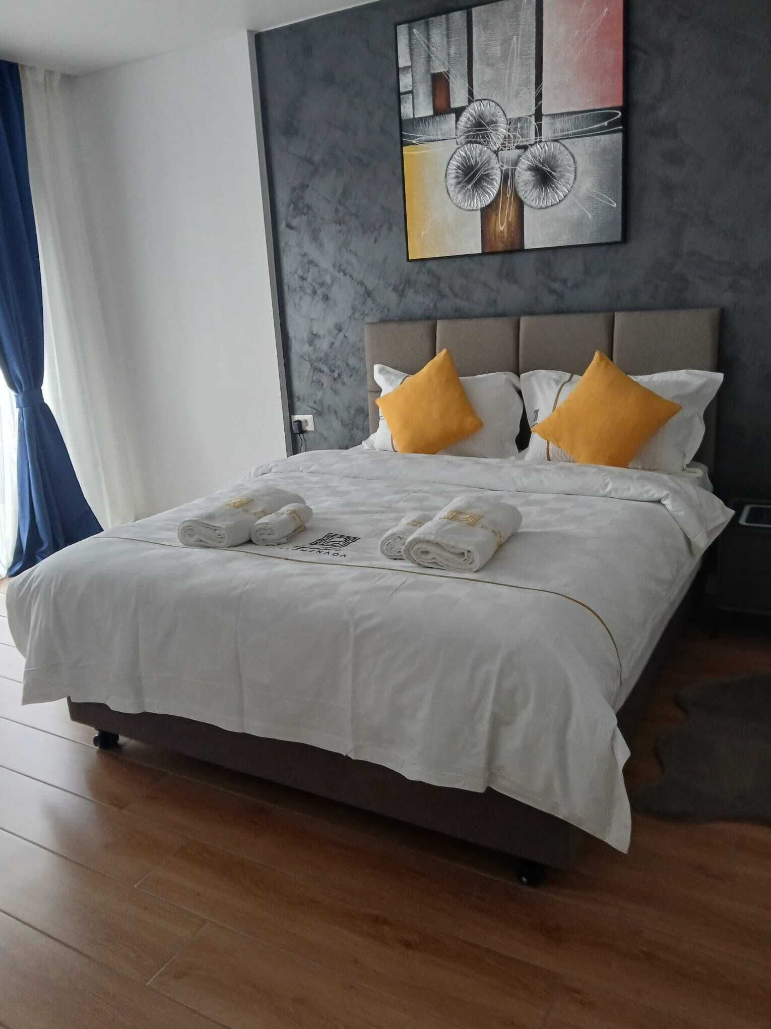 A hotel room with a bed, white bedding, two yellow pillows, and a painting on the wall.