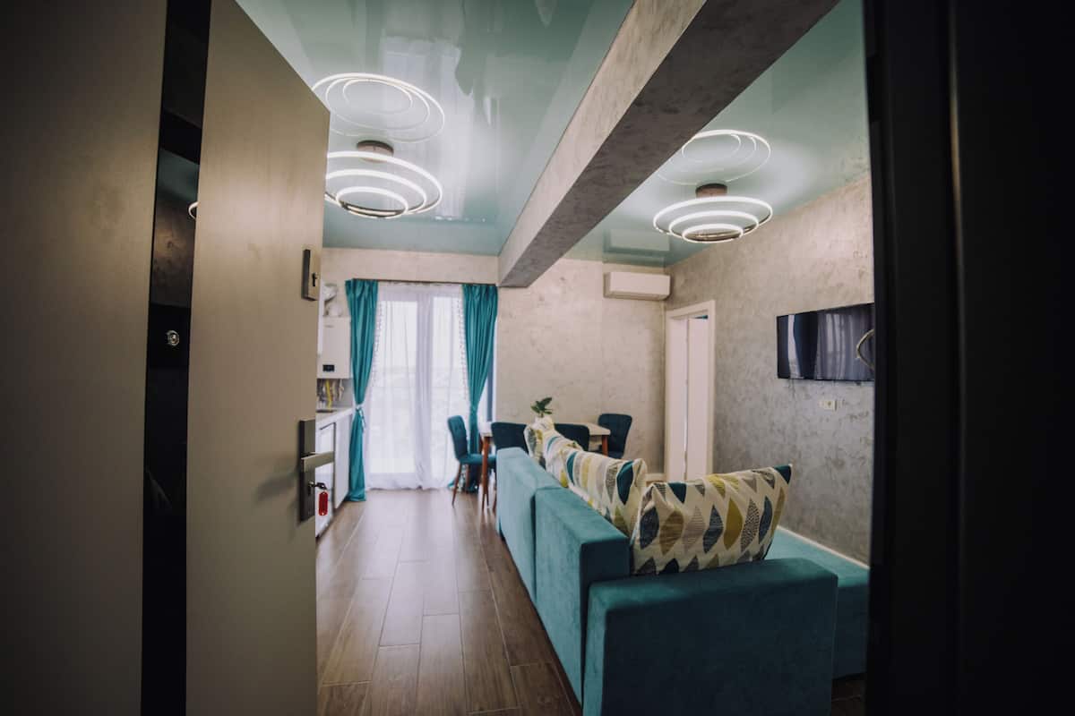 Un salon moderne avec un canapé, un téléviseur fixé au mur et un coin repas comprenant des chaises et une table.