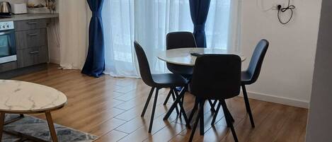 Una cocina moderna con horno empotrado, un comedor con una mesa redonda y cuatro sillas, y un amplio ventanal con cortinas azules.
