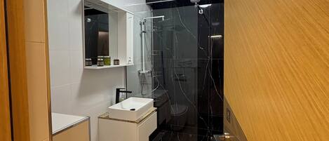 A modern bathroom with a glass shower enclosure, a white sink, and a toilet.