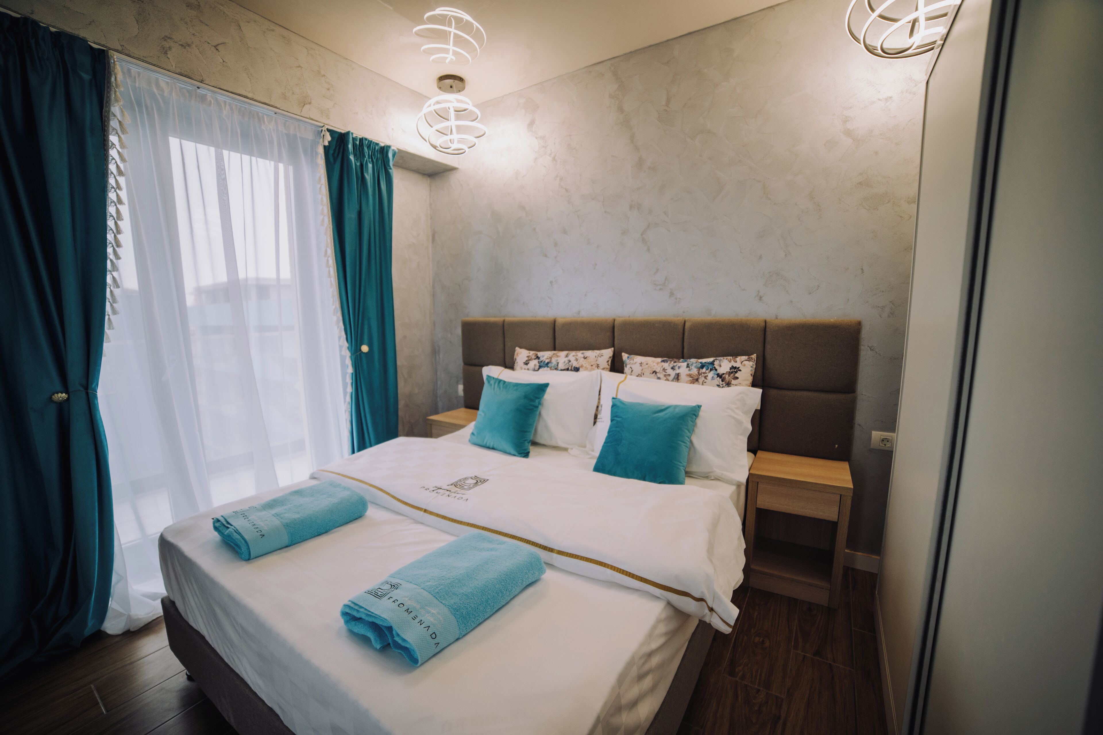 Ein Hotelzimmer mit Bett, Nachttisch, Lampe und einem Fenster mit Vorhängen.