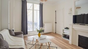 Ett modernt vardagsrum med en soffa, ett litet bord med en vas, en öppen spis och en tv.