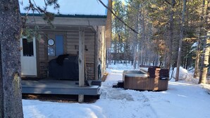 Eine Hütte mit Veranda, Whirlpool und einem schneebedeckten Garten.