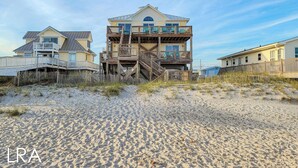 A beachfront house with multiple levels, a wooden deck, and a sandy beach in the foreground. - Buccaneers Bounty: Your Oceanfront Treasure Awaits (North Topsail Beach)