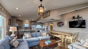 A spacious living room with a large sectional sofa, a wooden coffee table, and a dining area with a large table and chairs. - Buccaneers Bounty: Your Oceanfront Treasure Awaits (North Topsail Beach)