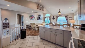 A spacious kitchen with a large island, wooden dining table, and a view of the ocean. - Buccaneers Bounty: Your Oceanfront Treasure Awaits (North Topsail Beach)