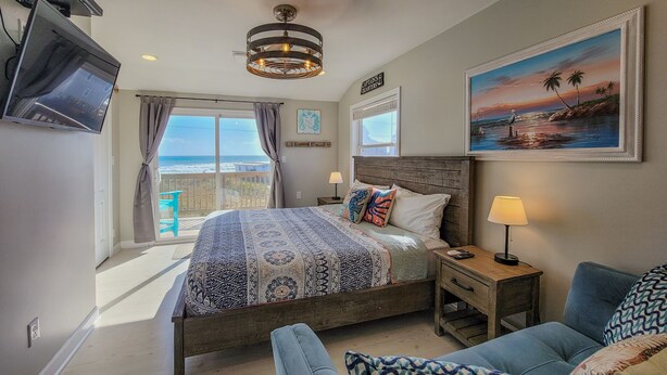 A bedroom with a large bed, a nightstand, a chair, a painting, and a TV. - Buccaneers Bounty II: Enjoy Stunning Ocean Views (North Topsail Beach)
