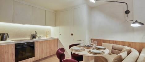 A modern kitchen with a built-in oven, a dining table set for four, and a cozy seating area with a sofa and chairs.