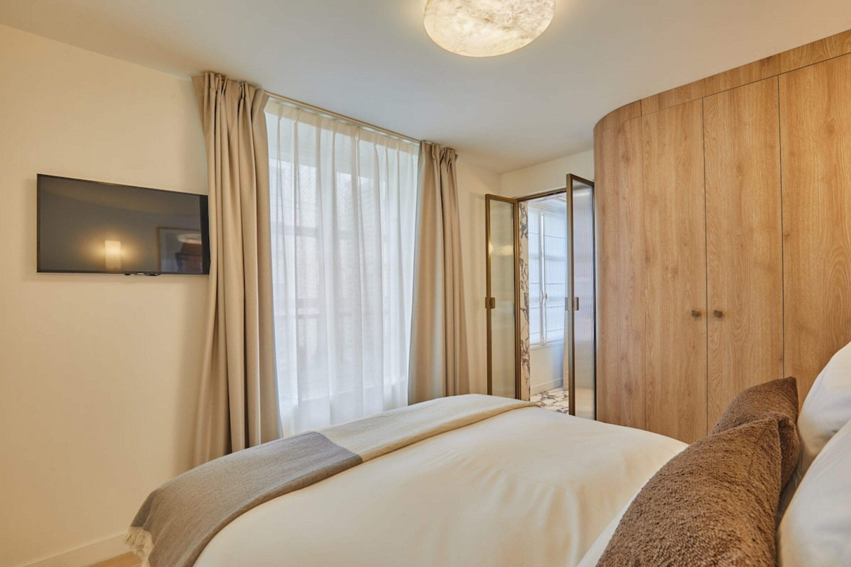 Ein modernes Schlafzimmer mit einem großen Bett, einem flachbildfernseher an der Wand und einem Holzschrank.