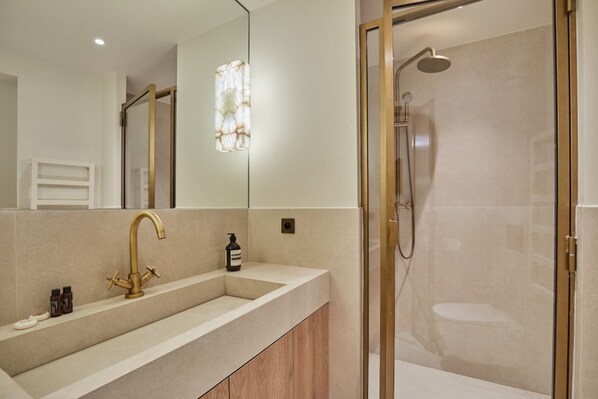 Une salle de bain moderne avec un grand miroir, un robinet doré et une douche à l’italienne.