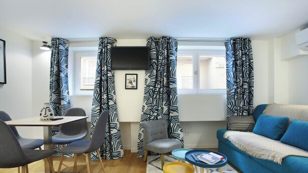 A modern living room with a blue sofa, a dining table with chairs, and patterned curtains. - Sublime and new Apartment Le Marais / Beaubourg (Paris)