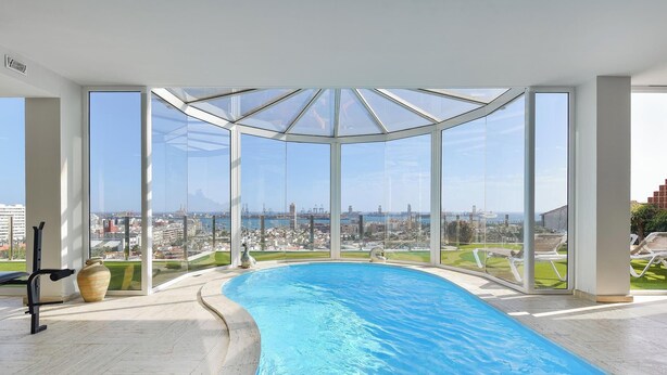 A modern indoor swimming pool with a panoramic city view through large windows.
