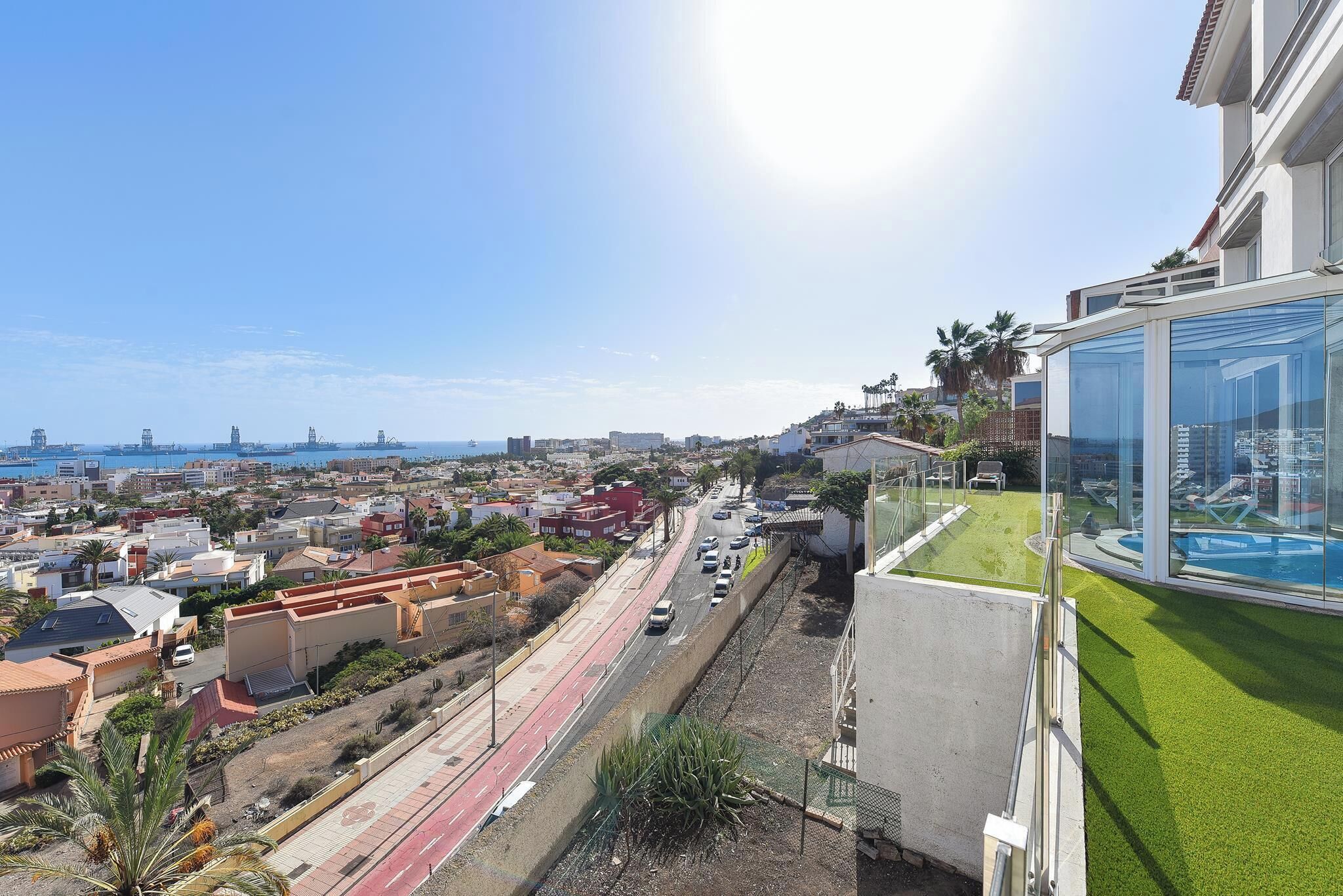 A residential area with a road, buildings, and a clear view of the sea.