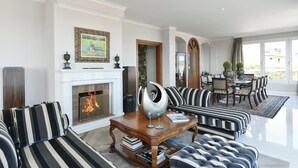 A living room with a fireplace, striped sofas, a coffee table, and a dining area with a chandelier.