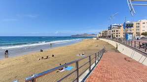 A beach with a paved walkway and a metal railing.