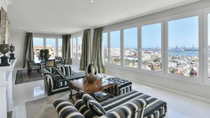 A spacious living room with a large window offering a city view, a dining area with a table and chairs, and a sofa set.