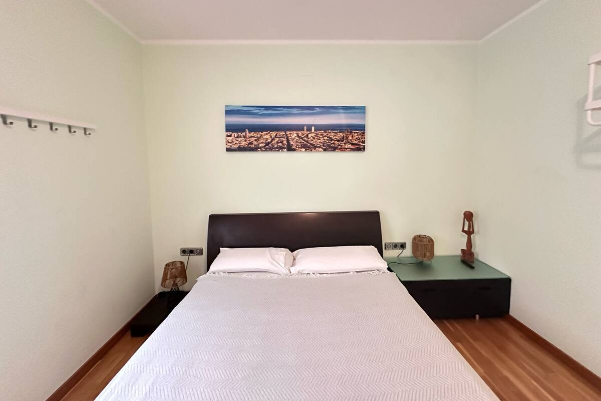 Ein ordentlich eingerichtetes Schlafzimmer mit einem Bett, einem Nachttisch, einer Lampe und einem an der Wand befestigten Bild.