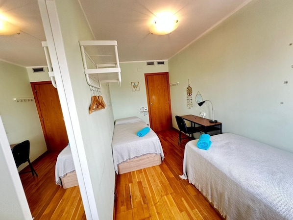 A small, compact room with two single beds, a desk, and a chair. There is a ceiling fan and a wall-mounted shelf with clothes. - Rooms Aribau 133 (Barcelona)