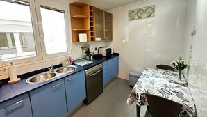 A compact kitchen with a sink, microwave, and stove, a dining table with a patterned tablecloth, and a window with blinds. - Rooms Aribau 133 (Barcelona)