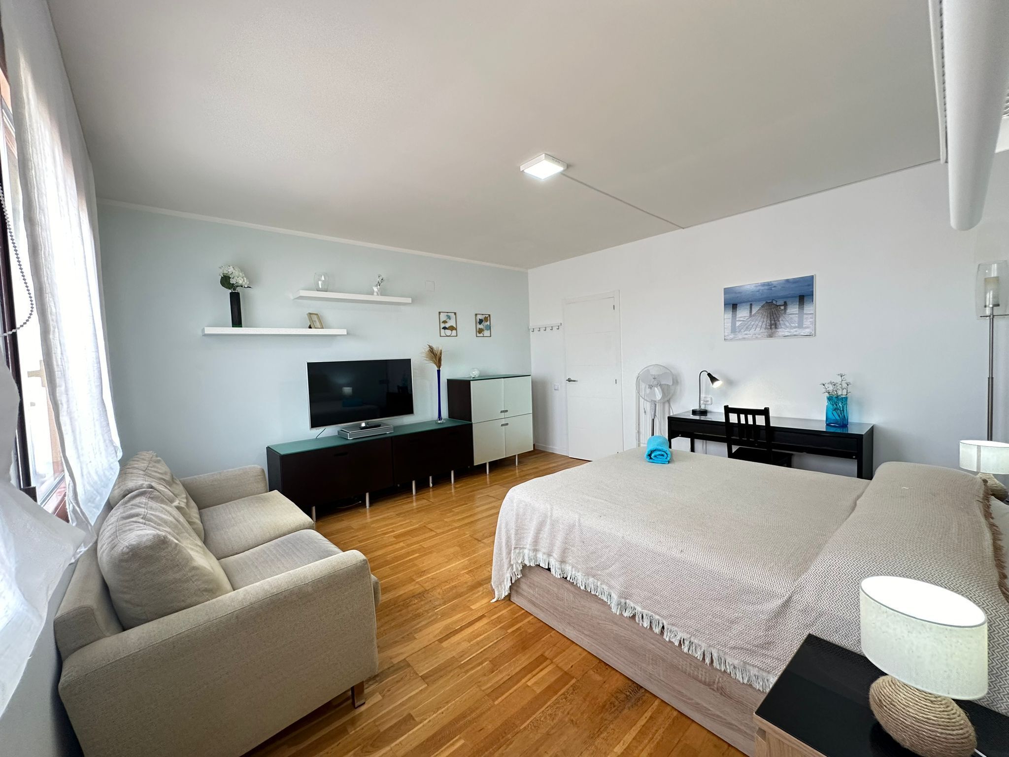 Un dormitorio moderno con cama, televisor, escritorio y sofá.