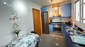 A compact kitchen with a refrigerator, stove, and sink. A decorative wall sign reads "ALL YOU NEED IS coffee." - Rooms Aribau 133 (Barcelona)