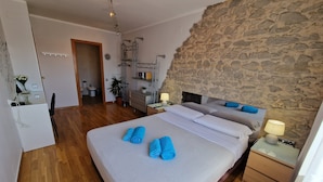 A bedroom with a large bed, wooden flooring, a stone accent wall, a desk with a lamp, and a bathroom visible in the background. - Rooms Aribau 133 (Barcelona)