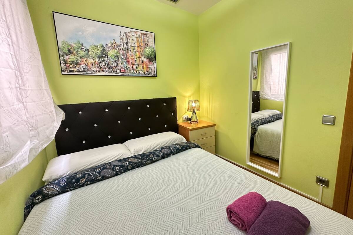 Ein Hotelzimmer mit Bett, Nachttisch, Lampe, Spiegel und einem Bild an der Wand.
