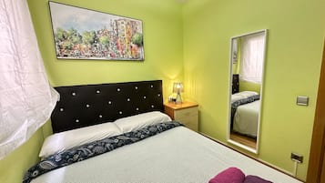 A hotel room with a bed, a nightstand, a lamp, a mirror, and a painting on the wall.
