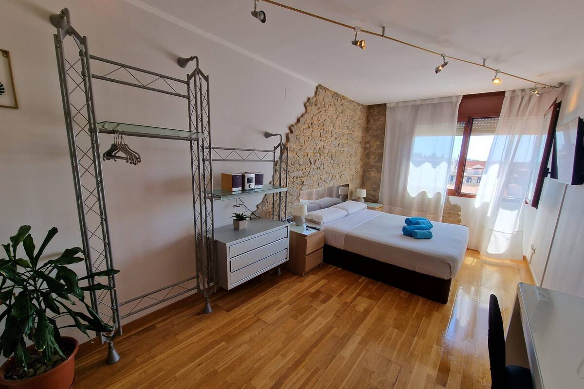Ein Schlafzimmer mit Bett, Nachttischen, einem Schreibtisch, einer Topfpflanze und einer Steinsäule.