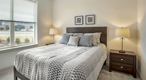 A bedroom with a bed, two bedside tables, a window, and two wall-mounted picture frames. - National at Occoquan River - Woodbridge (Woodbridge)