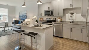 Una cocina moderna con armarios blancos, electrodomésticos de acero inoxidable, una isla central con taburetes y vistas al área de estar.