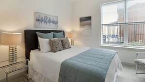 Un dormitorio moderno con una cama, dos lámparas de noche, una obra de arte con vista a un paisaje urbano y una ventana con persianas.