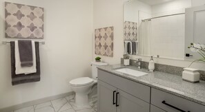 A modern bathroom with a toilet, sink, and mirror. There are towels hanging on a rack and a plant on the counter. - National at Occoquan River - Woodbridge (Woodbridge)