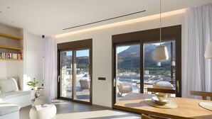 Un salon moderne comprenant un canapé, une table basse et un coin repas avec une table et des chaises. De grandes fenêtres offrent une vue sur l’extérieur.