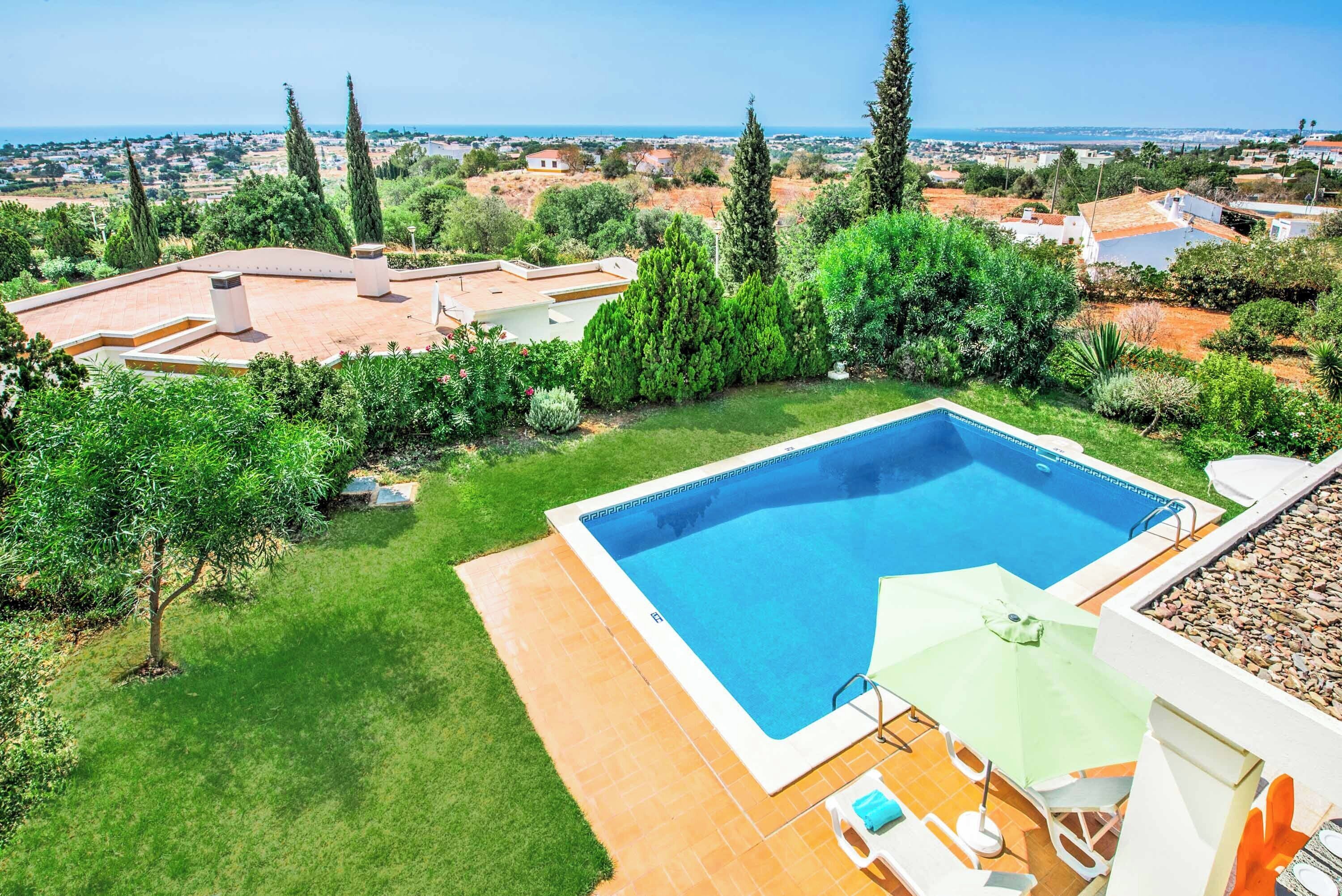 Piscina com vista para o mar, rodeada por vegetação e um terraço revestido com azulejos.