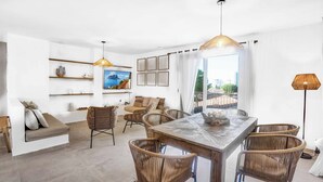 A modern living room with a dining area, featuring wicker furniture, a wooden table, and a large window with a city view. - Brisa y Mar - Six Bedroom Villa, Sleeps 12 (Calp)