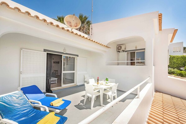 A balcony with blue lounge chairs, a table with chairs, and a sliding glass door.