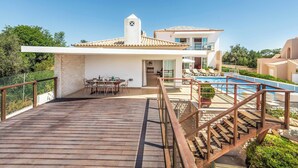 A modern villa with a wooden deck, a swimming pool, and a dining area.
