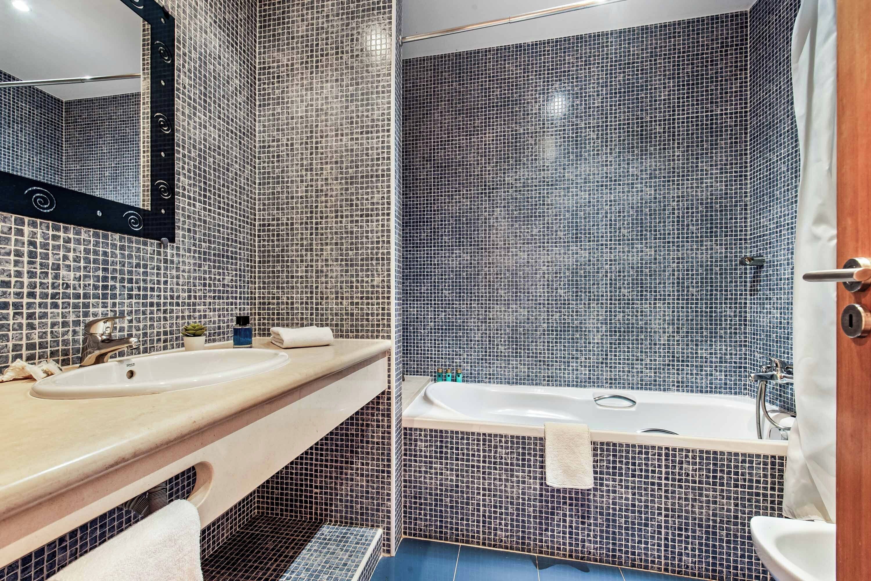 A bathroom with a sink, mirror, and bathtub.