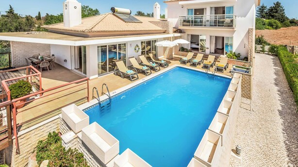 A modern two-story house with a swimming pool, outdoor seating, and a view of the surrounding landscape.