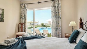 A hotel room with a bed, a view of a swimming pool, and a chair by the window.