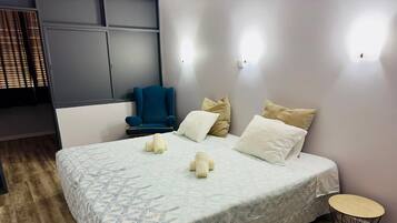Habitación de hotel ordenada con una cama grande, una silla y una mesita redonda.