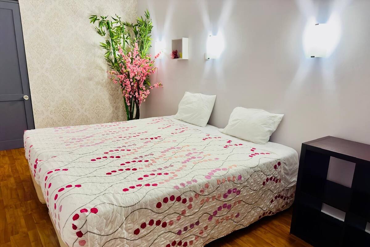 A neatly made bed with a floral-patterned bedspread, a small bedside table, and a wall-mounted light fixture.