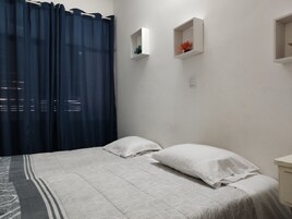 A bedroom with a bed, white curtains, and two wall-mounted shelves with decorative items.