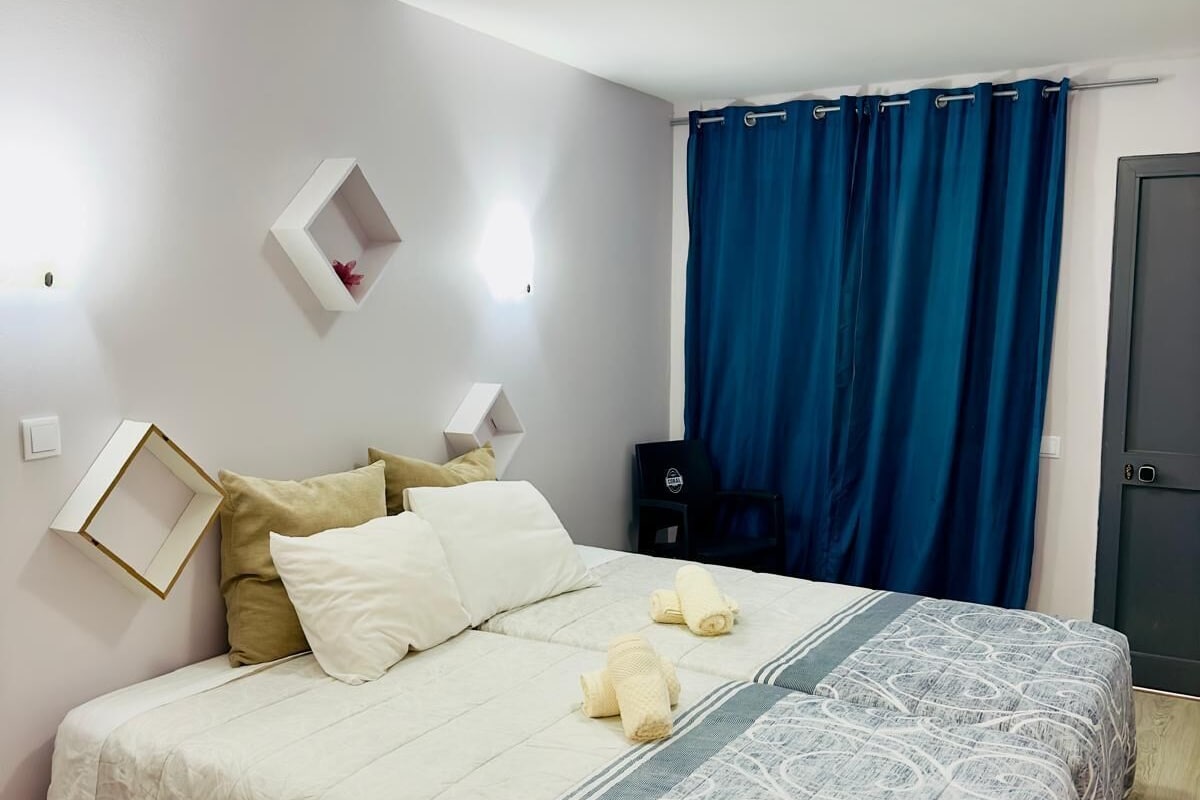 A bedroom with a bed, a bedside table, a wall-mounted shelf, and a door.
