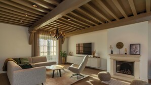 A spacious living room with a sofa, armchair, and coffee table, a fireplace, and a TV mounted on the wall.